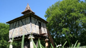 Een stenen toren met een kegelvormig dak, gedragen door houten pilaren, omgeven door weelderige begroeiing.