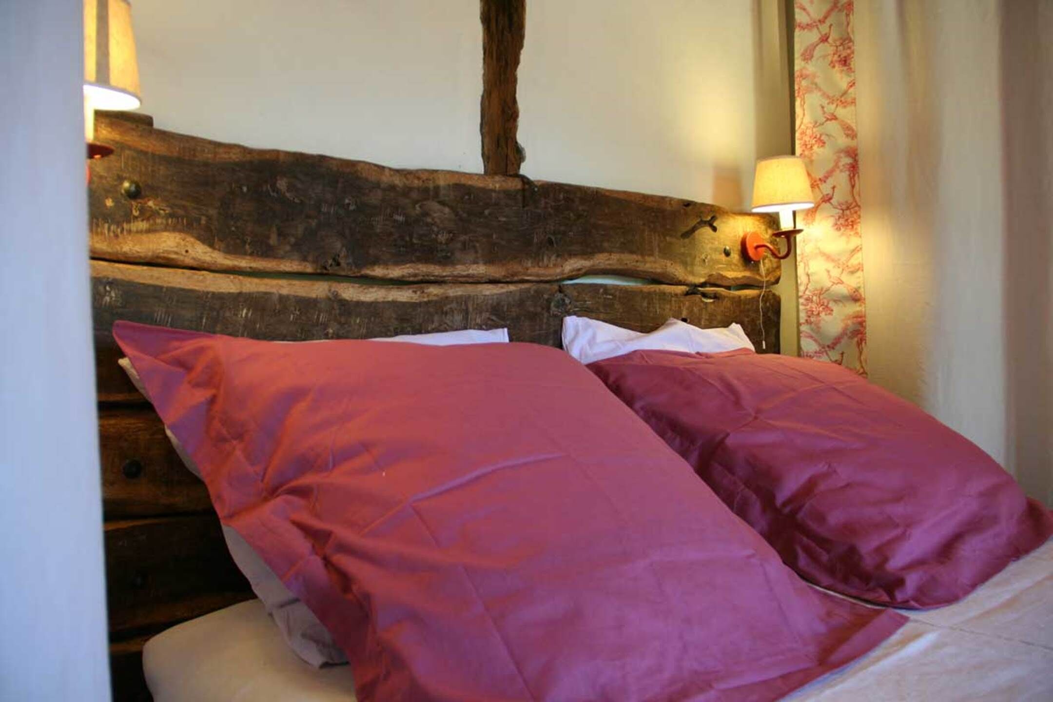 Een bed met een houten hoofdbord, twee kussens en een wandlamp.