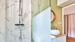 Une salle de bain dotée d’une douche à parois de verre, d’un mur recouvert de carreaux de marbre, d’un lavabo avec un plan de toilette en bois et d’un miroir agrémenté d’un vase à fleurs.