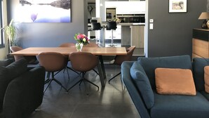 Un salon moderne avec un coin repas, comprenant un grand téléviseur à écran plat, un canapé bleu et une table à manger en bois avec quatre chaises.