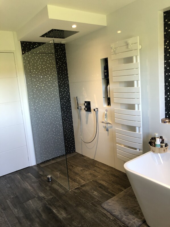 Un baño moderno con cabina de ducha de vidrio, una bañera blanca y un tapete de baño de madera.