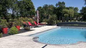 Une piscine bordée de chaises longues rouges et agrémentée de plantes en pot.