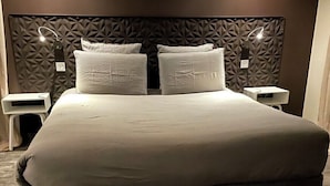 Un grand lit avec une tête de lit à motifs géométriques, deux tables de chevet avec des lampes et une chambre aux couleurs neutres.