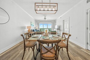 Un coin repas avec une table et des chaises en bois, un lustre et une vue sur l’extérieur par une fenêtre.