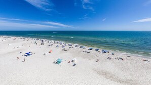 A wide beach with numerous umbrellas and beach chairs, a clear blue sky, and calm sea. - Top-Rated Comfort – Guest-Praised "Nicest unit" – Gulf Front – Two King Beds (Gulf Shores)