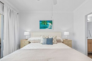 A bedroom with a large bed, two bedside tables, a nightstand, a painting of a beach scene, and a mirror on the wall. - CSW206 – Top-Rated Comfort – Guest-Praised "Nicest Unit" – Gulf Front – 2 Kings (Gulf Shores)
