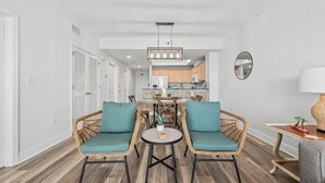 A modern living room with wicker chairs, a round coffee table, and a dining area in the background. - Top-Rated Comfort – Guest-Praised "Nicest unit" – Gulf Front – Two King Beds (Gulf Shores)