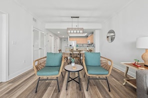 A modern living room with wicker chairs, a round coffee table, and a dining area in the background.