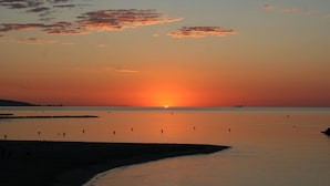 Un atardecer sobre un mar tranquilo con siluetas de personas y barcos.