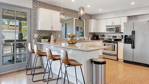 A modern kitchen with a central island, bar stools, stainless steel appliances, and a patterned backsplash. - Nova Gypsy Vanner | Pool | Spacious Interior (Scottsdale)