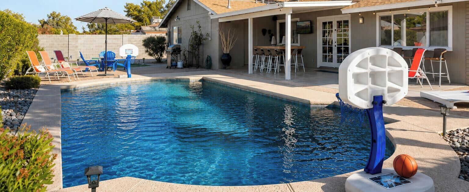 En swimmingpool med liggestole, en basketballkurv og en overdækket terrasse.