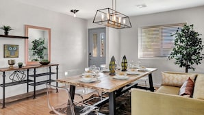 A dining area with a wooden table set for four, surrounded by chairs. There is a sofa with cushions, a potted plant, and a wall-mounted mirror. - Nova Gypsy Vanner | Pool | Spacious Interior (Scottsdale)