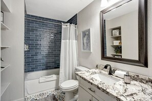 A bathroom with a white bathtub, a white toilet, a sink with a marble countertop, and a large mirror.