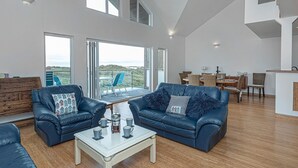 Een ruime woonkamer met twee blauwe leren banken, een salontafel, en een eethoek met stoelen en een tafel.