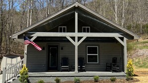 Eine zweistöckige Holzhütte mit Veranda, einer Flagge und einem kleinen Garten.