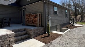 Ein zweistöckiges Haus mit überdachter Veranda, einem Holzstapel und einem Schotterweg.