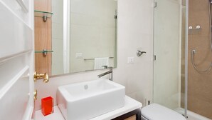 Een moderne badkamer met een witte wastafel, een glazen douchecabine en een houten opbergmeubel.