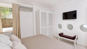 Een slaapkamer met een bed, een aan de muur bevestigde televisie, een kledingkast en een bankje met een spiegel.