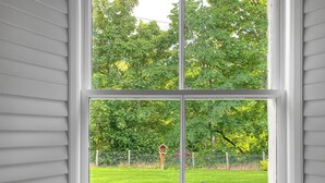 A large window with a view of a backyard, including a lawn, a wooden birdhouse, and a fence.