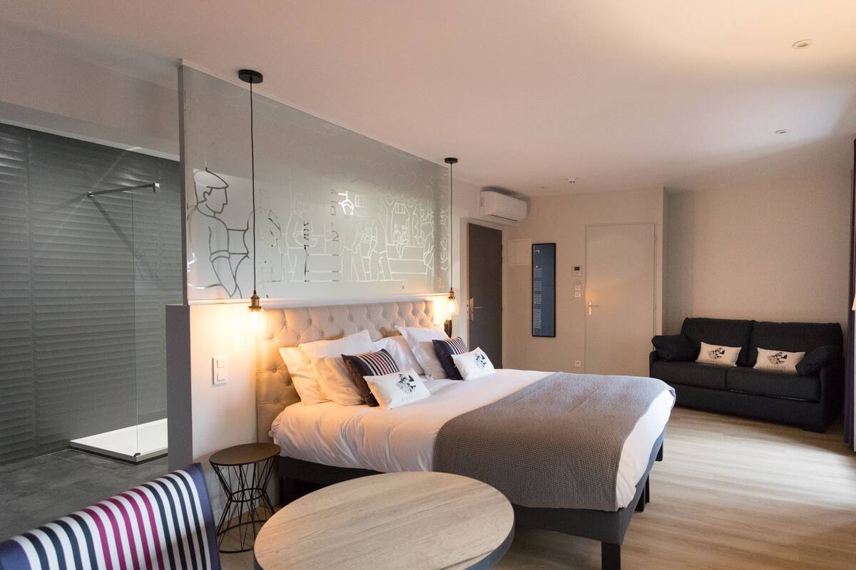 A modern hotel room with a bed, bedside table, sofa, and a lamp.