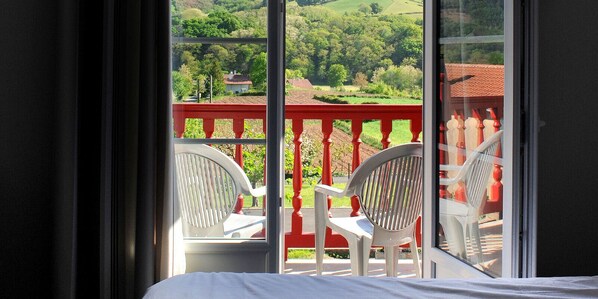 A balcony with two white chairs and a red railing overlooking a green landscape.
