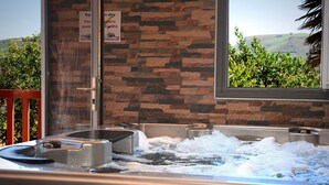 A spa area with two hot tubs, a wooden railing, and a view of greenery through a window.