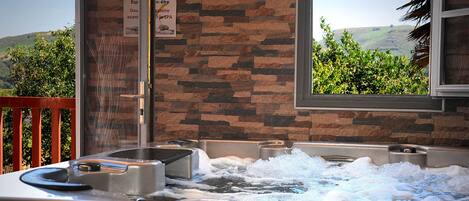 A spa area with two hot tubs, a wooden railing, and a view of greenery through a window.