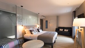 A modern hotel room with a large bed, a sofa, a small round table, and a lamp.