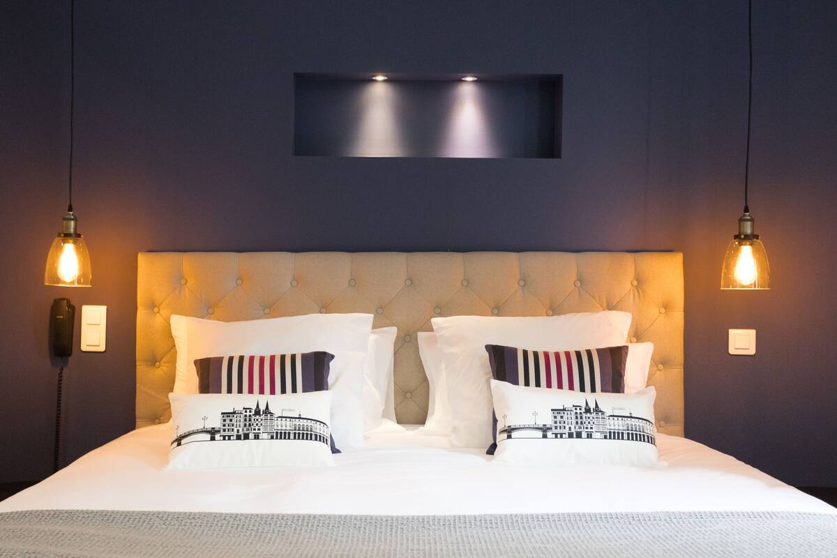 A neatly made bed with a tufted headboard, two bedside lamps, and a wall-mounted light fixture above.