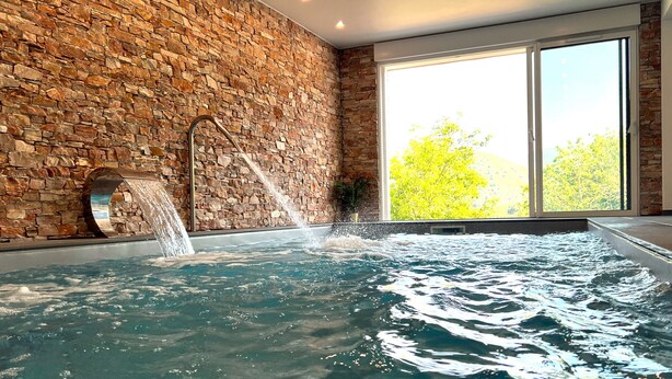 A spa area with a stone wall, a hot tub, and a window with a view of trees.