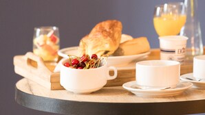 A breakfast setting with a croissant, a bowl of cherries, a glass of orange juice, and a cup on a wooden table.
