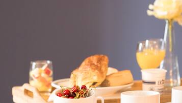 A breakfast setting with a croissant, a bowl of cherries, a glass of orange juice, and a cup on a wooden table.