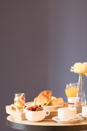 A breakfast setting with a croissant, a bowl of cherries, a glass of orange juice, and a cup on a wooden table.