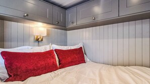 A bed with white and red pillows, a wall-mounted light, and wooden paneling.