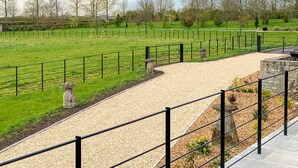 A gravel path leading to a grassy field with a fence, stone pillars, and a stone wall.
