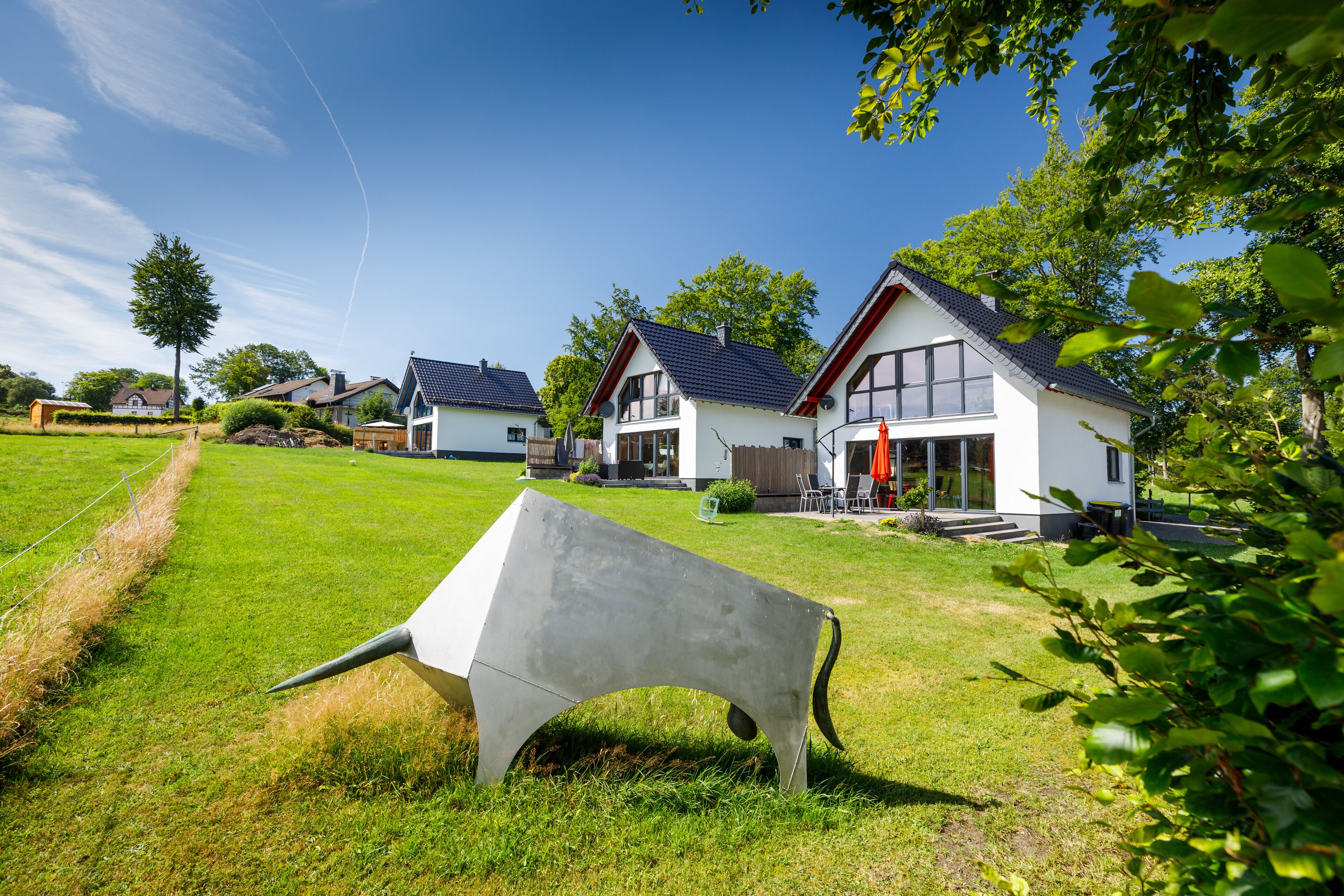 Una zona residencial con casas modernas, un césped y una gran escultura de concreto.