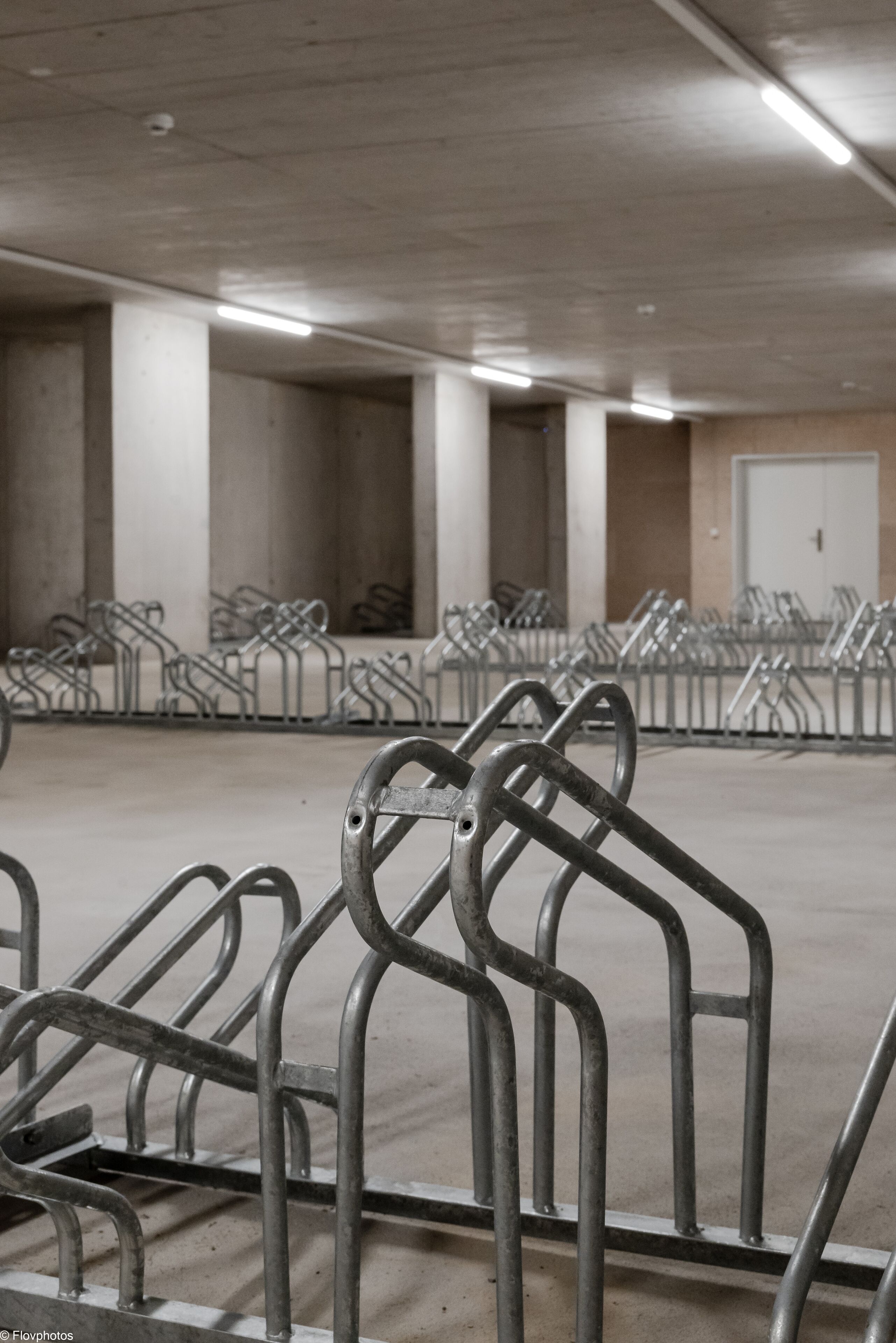 Een parkeergarage met rijen metalen fietsenrekken en betonnen pilaren.