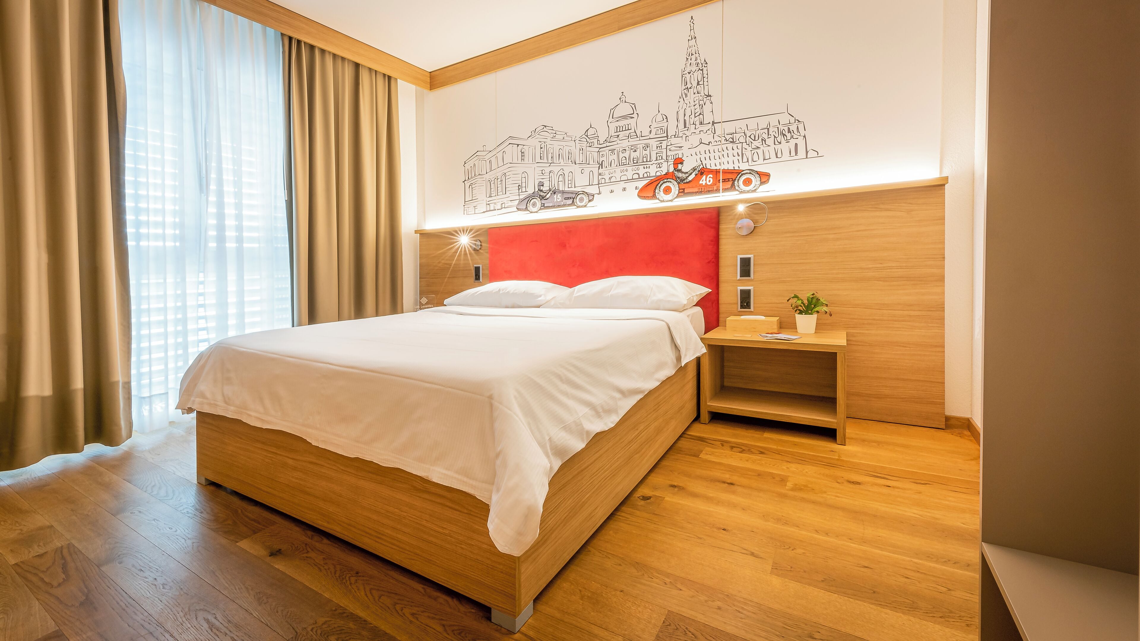A modern hotel room with a wooden bed, a red accent wall, and a cityscape mural.