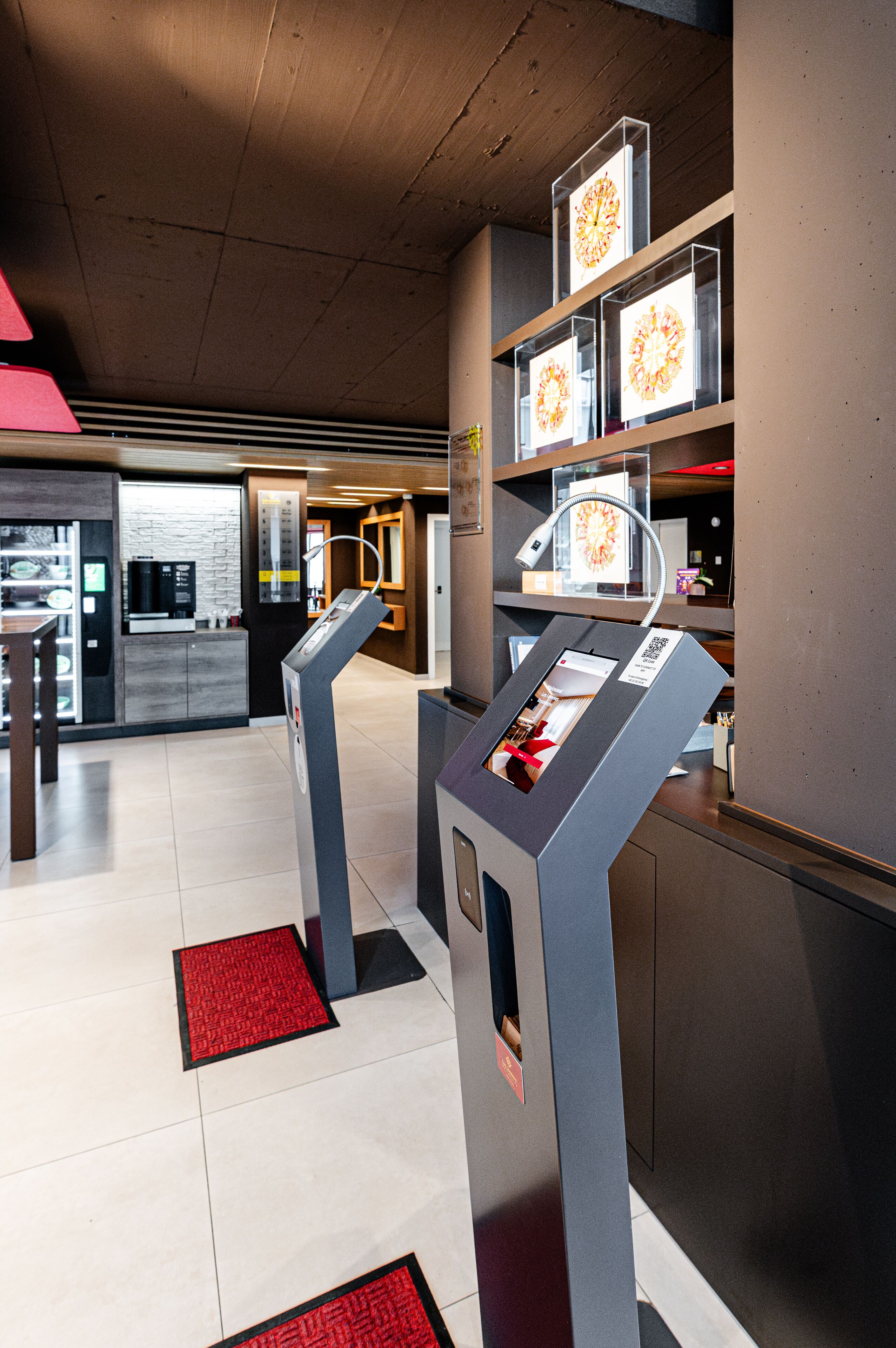 En modern hotellobby med en självbetjäningskiosk, en receptionsdisk och en sittgrupp.