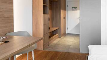 Una moderna camera d'albergo con pavimento in legno, un letto, una scrivania con una sedia e scaffalature a muro in legno.