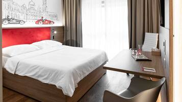 A hotel room with a bed, a desk, a chair, a flat-screen TV, and a wall mural.