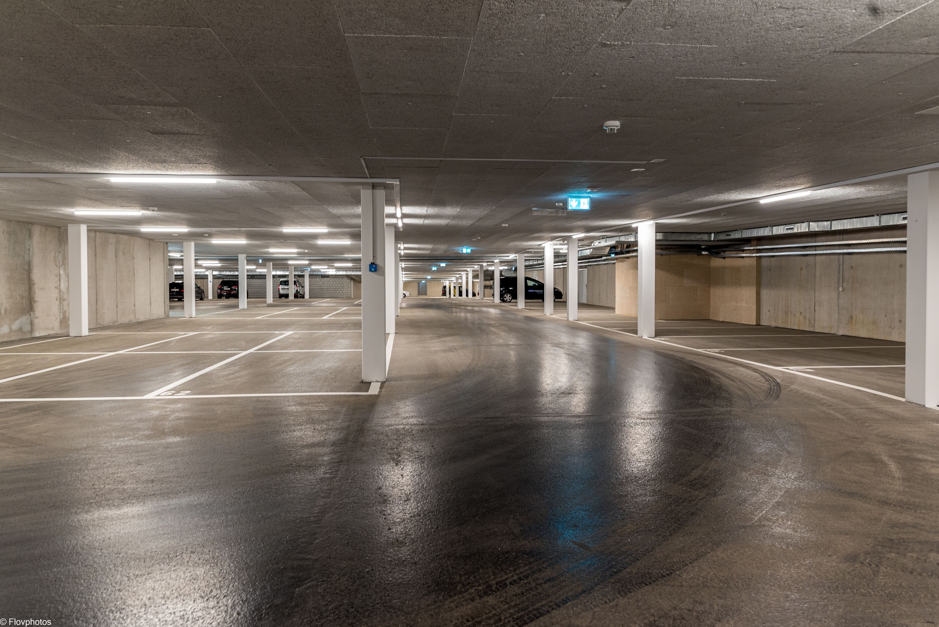 Un estacionamiento interior con pilares de concreto, espacios delimitados y iluminación en el techo.
