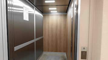 An elevator interior with a metallic finish, a wooden panel wall, and a tiled floor.