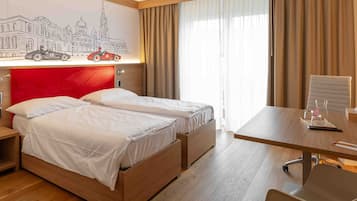 Ein Hotelzimmer mit Holzboden, einem Bett mit rotem Kopfteil, einem Schreibtisch mit Stuhl und einem großen Fenster mit Vorhängen.