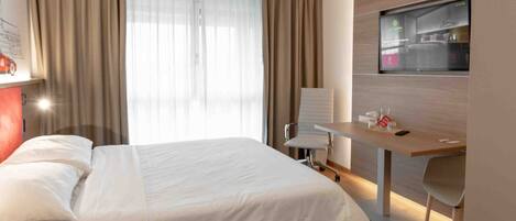 A modern hotel room with a wooden bed, a desk, and a TV on the wall.
