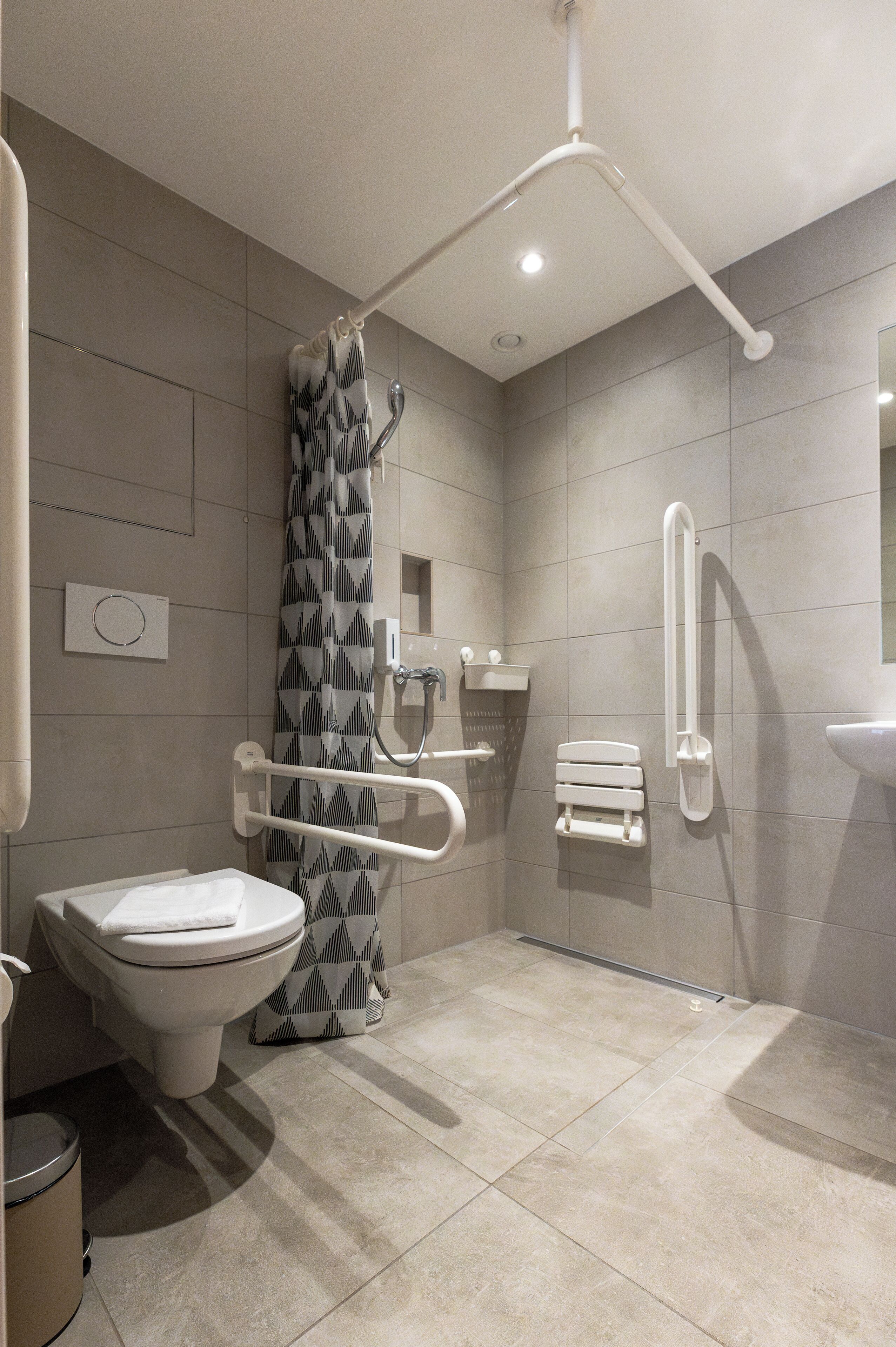 Un baño moderno con inodoro, bidé y zona de ducha, equipado con barras de apoyo y ducha de seguridad.