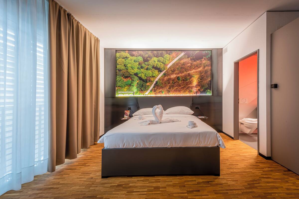A modern hotel room with a large bed, a TV on the wall, and a wooden floor.