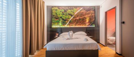 Une chambre d’hôtel moderne avec un grand lit, un téléviseur fixé au mur et un plancher en bois.