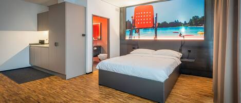 A modern hotel room with a bed, a desk, and a large window with a beach view.