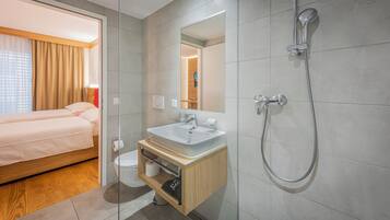 A modern hotel room with a wooden bed, a white bathroom with a sink and shower, and a large mirror.